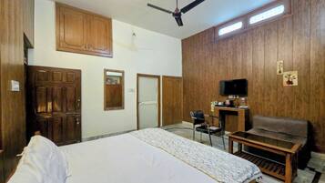 A bedroom with a bed, a desk, a chair, a television, and a ceiling fan.