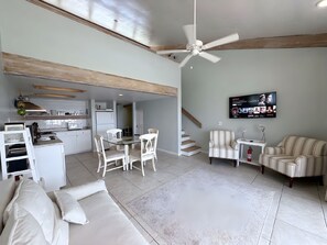 Ein geräumiger Wohnbereich mit Esstisch, Stühlen, einer Couch, einem an der Wand befestigten Fernseher und einem Deckenventilator.