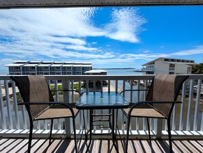 Un balcon avec une table et des chaises, donnant sur une étendue d’eau et des bâtiments.