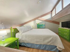 Une chambre à coucher avec un lit, un fauteuil vert, une table de chevet, une commode et un tableau accroché au mur.