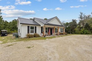 A two-story house with a porch and a gravel driveway. - Shelly's Chateau- Coastal Farmhouse w/ Fenced Yard (Cedar Key)