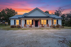A two-story house with a front porch, a covered patio, and a gravel driveway. - Shelly's Chateau- Coastal Farmhouse w/ Fenced Yard (Cedar Key)