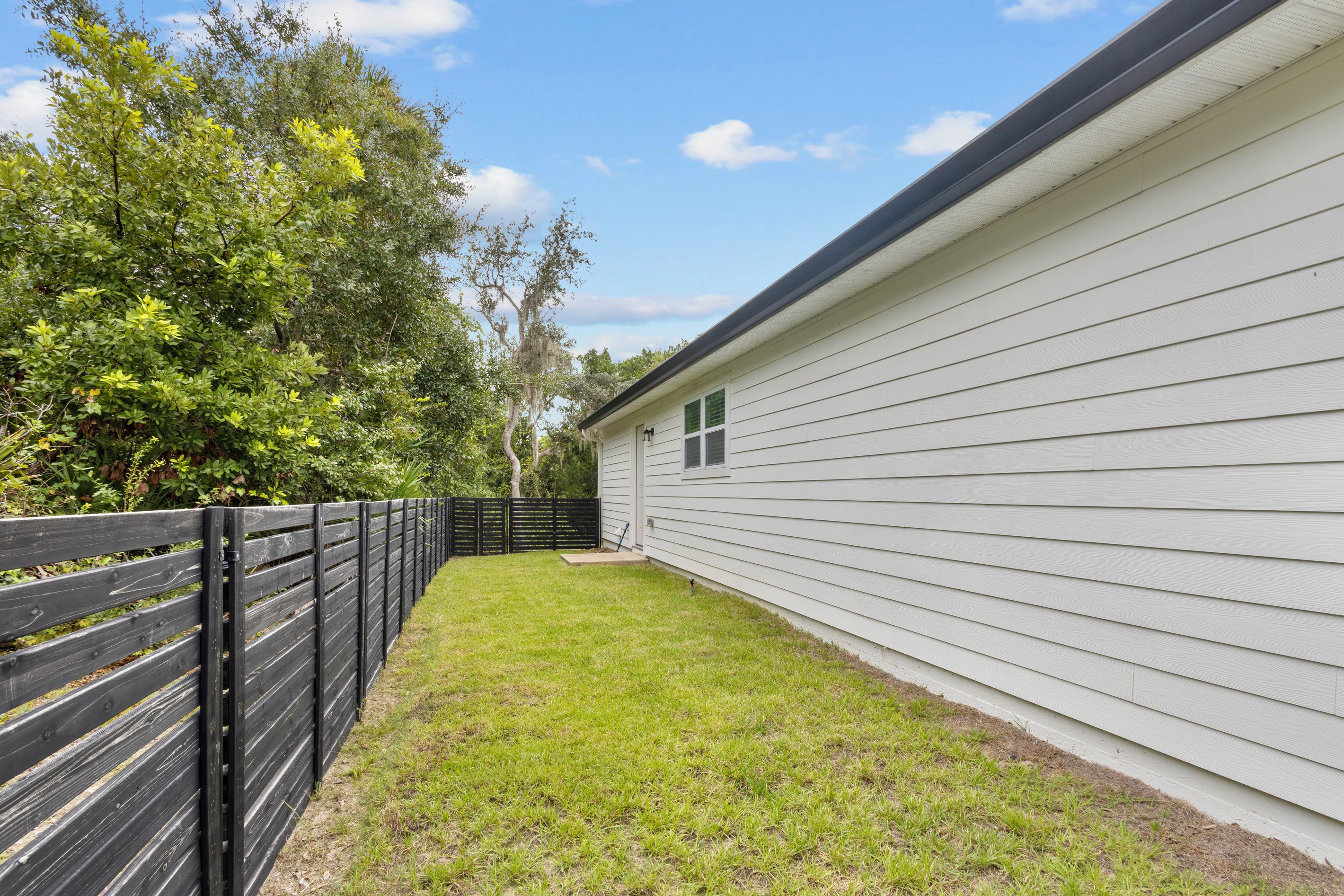 A fenced backyard with a grassy area and a white building with a window.