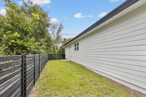 A fenced backyard with a grassy area and a white building with a window. - Shelly's Chateau- Coastal Farmhouse w/ Fenced Yard (Cedar Key)