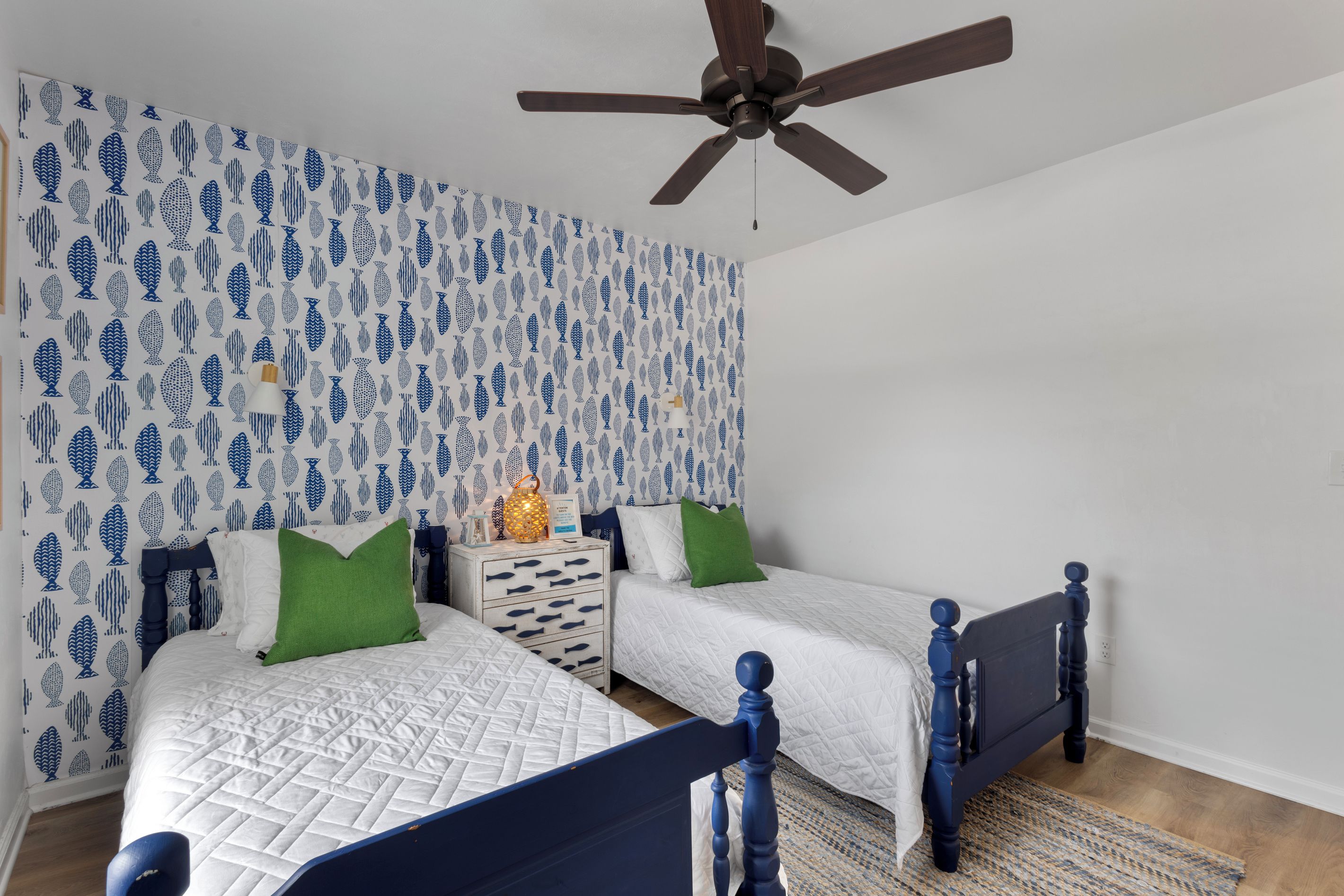 A bedroom with two beds, a ceiling fan, and a patterned wallpaper.