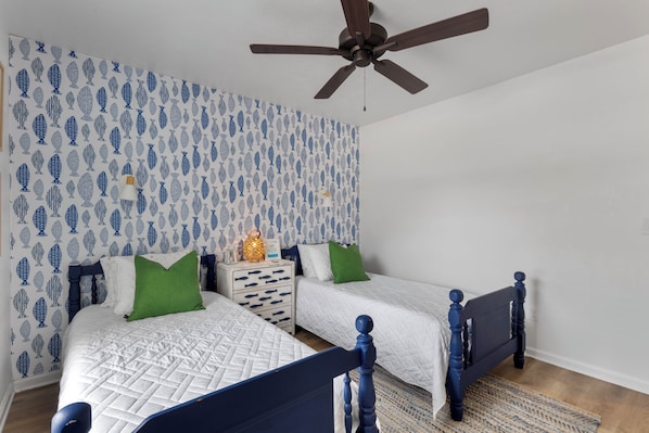 A bedroom with two beds, a ceiling fan, and a patterned wallpaper.