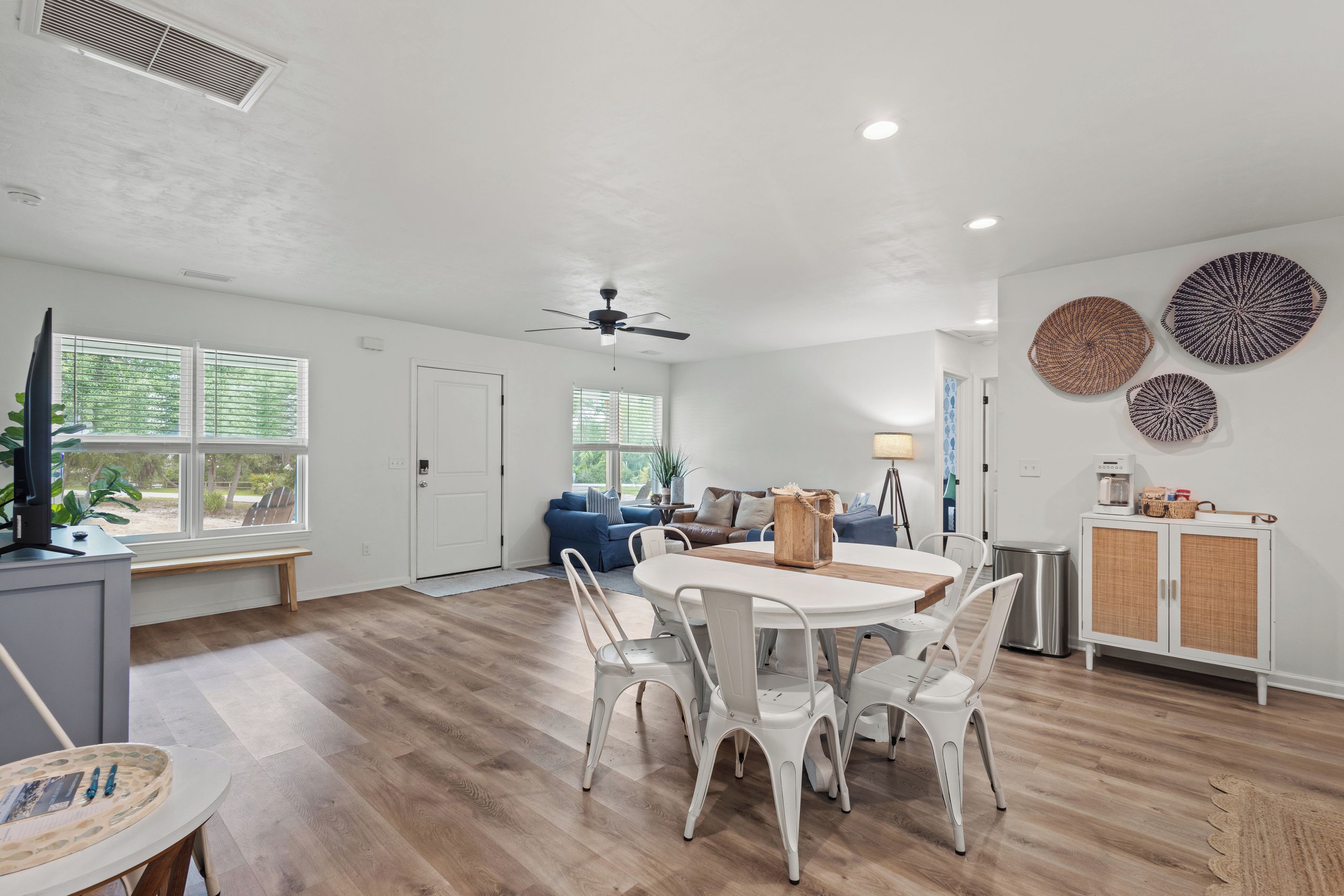 A spacious living area with a dining table and chairs, a ceiling fan, and a view of the outdoors through large windows.