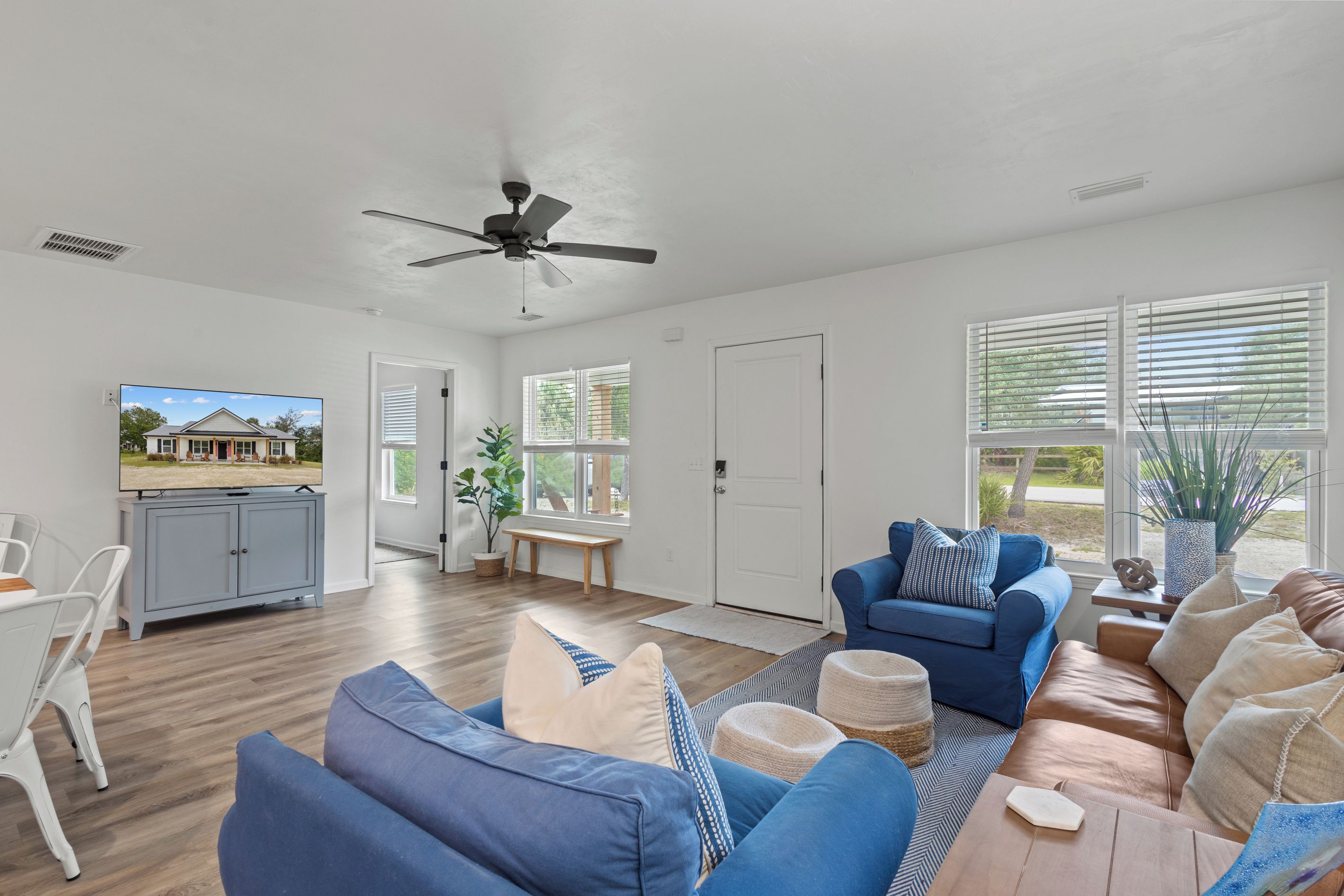 A spacious living room with a ceiling fan, a television, and a view of a house through the window.