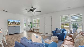 A spacious living room with a ceiling fan, a television, and a view of a house through the window.