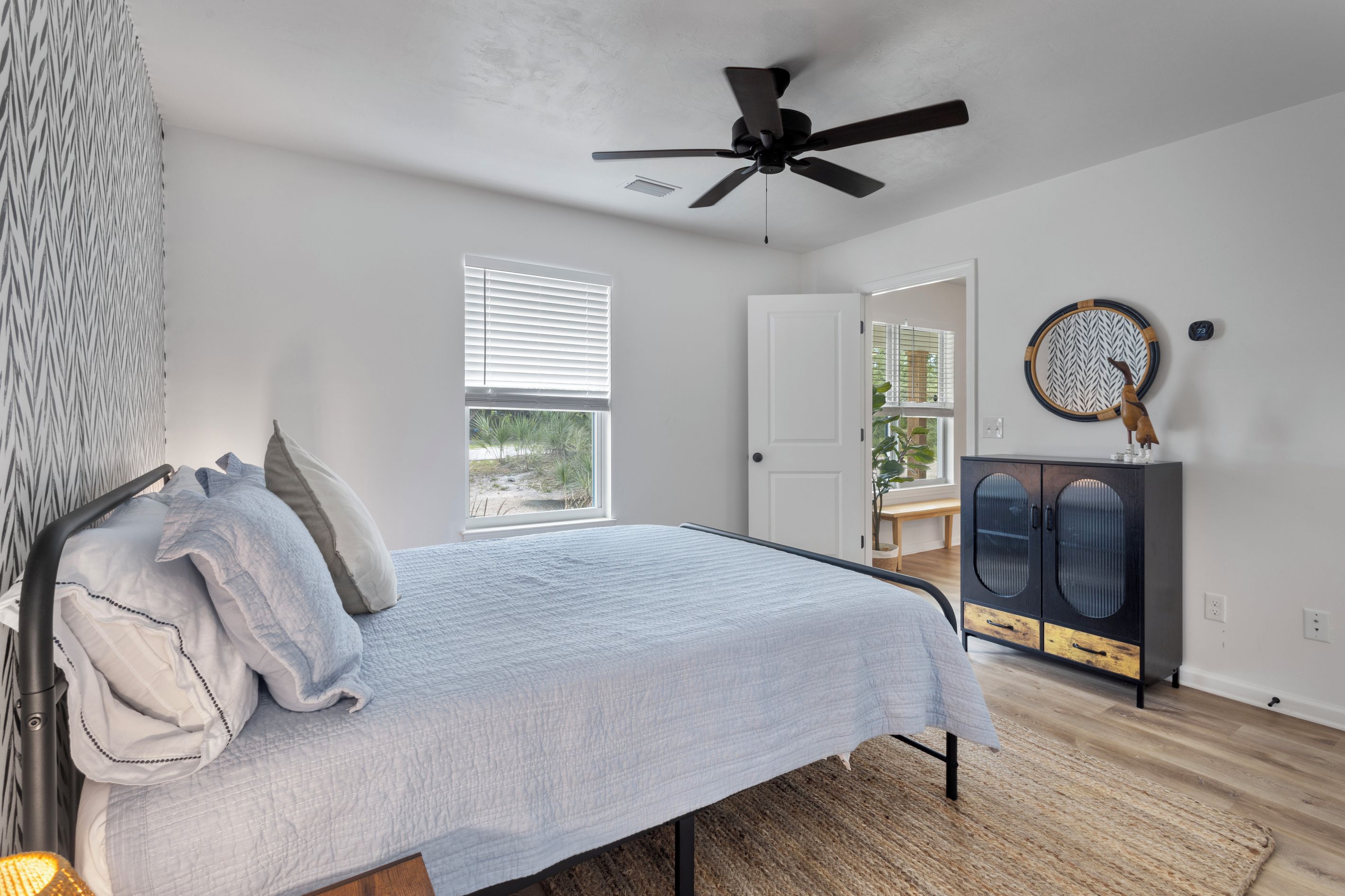 A bedroom with a bed, a ceiling fan, a window with blinds, a door, a cabinet, and a wall clock.