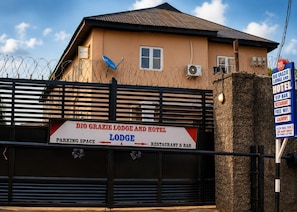 Entrada com portão para o DIO Grazie Lodge e Hotel, com placa indicando espaço de estacionamento, lodge e áreas de restaurante e bar.