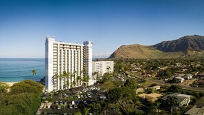A high-rise hotel with multiple floors, a parking lot, and a view of the ocean and mountains. - 
Amazing Ocean Views - Beachfront 2BR with AC at Hawaiian Princess Makaha Resort (Waianae)