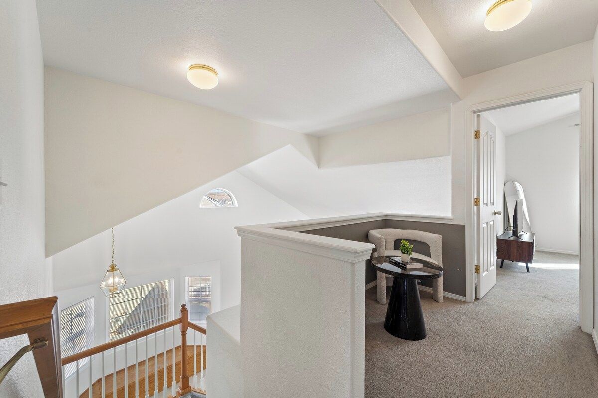 Un interior amplio con techo alto, una escalera que conduce a un nivel superior y una zona de estar con una pequeña mesa y sillas.