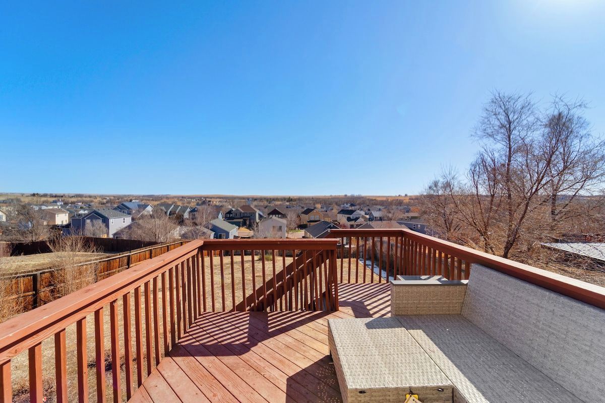 A wooden deck with a bench and a view of a residential area.
