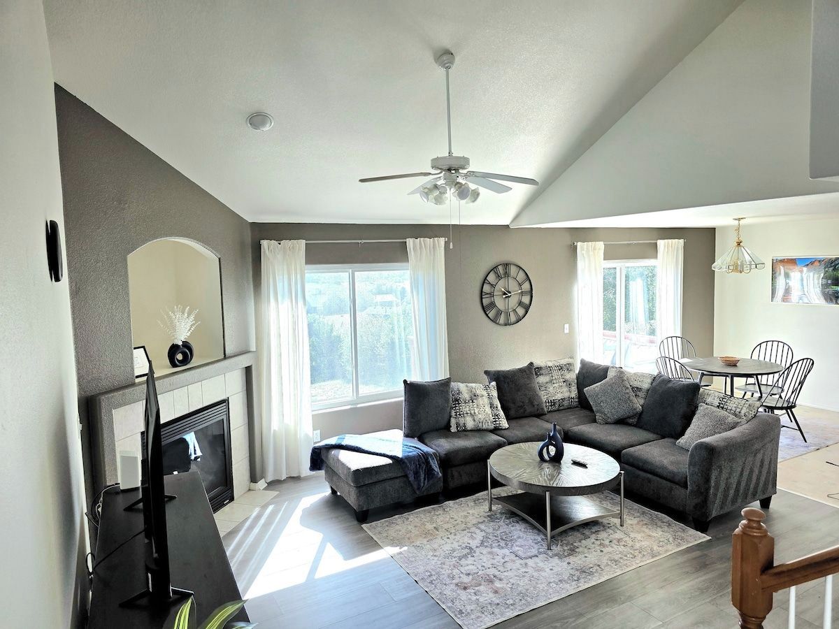 A modern living room with a fireplace, a sectional sofa, a round coffee table, and a dining area with chairs.