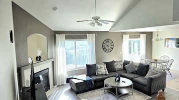 A modern living room with a fireplace, a sectional sofa, a round coffee table, and a dining area with chairs.