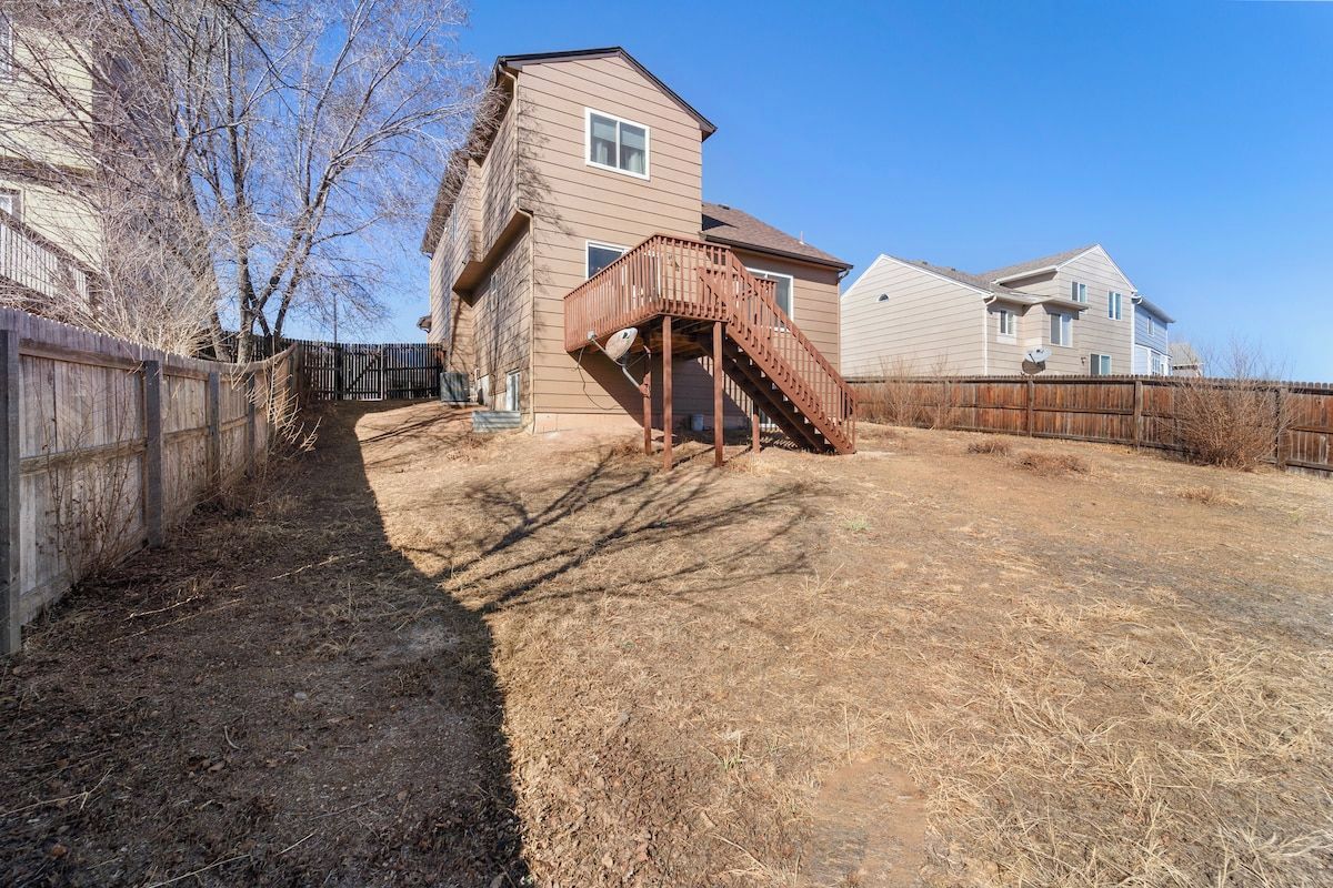 A residential backyard with a wooden deck, a fenced area, and a dry lawn.