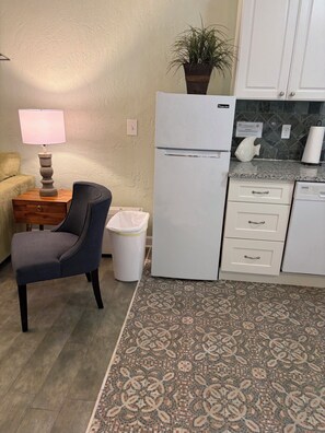 A compact kitchen with a refrigerator, a sink, a countertop, a chair, a trash bin, and a patterned rug. - Tranquil Studio cottage with pull-out sofa.  Sleeps 4. Cottage #1811 (Ruskin)