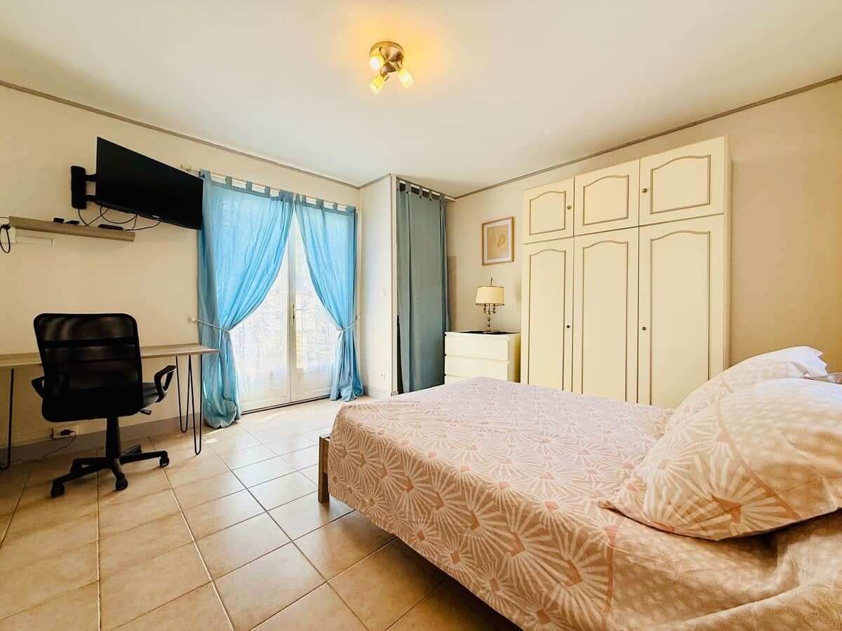 Ein Hotelzimmer mit einem Bett, einem Schreibtisch mit Stuhl, einem an der Wand befestigten Fernseher und einem Fenster mit Vorhängen.