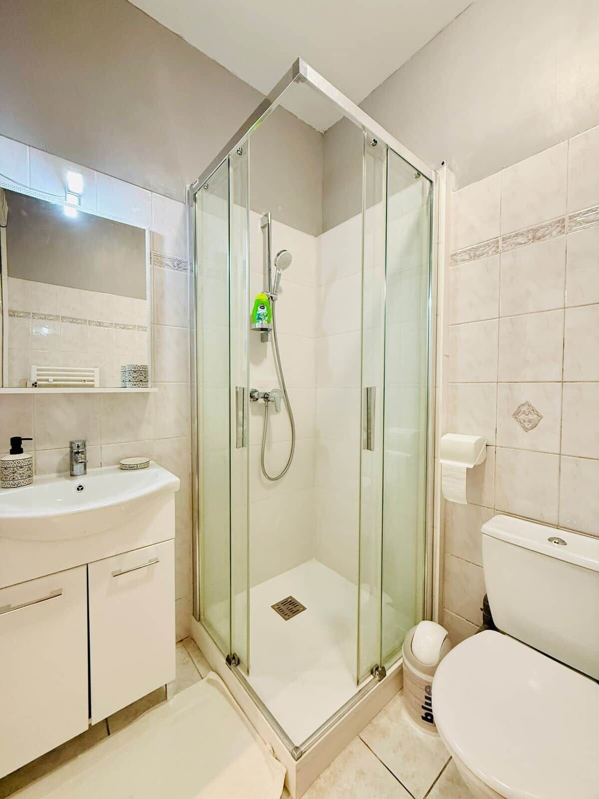 A modern bathroom with a glass-enclosed shower, a white sink with a soap dispenser, and a toilet.