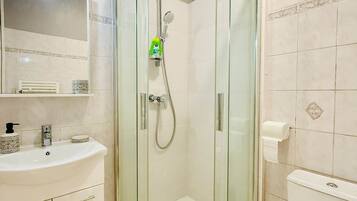 A modern bathroom with a glass-enclosed shower, a white sink with a soap dispenser, and a toilet.