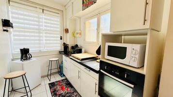 A compact kitchen with a microwave, oven, and a small dining area with stools.