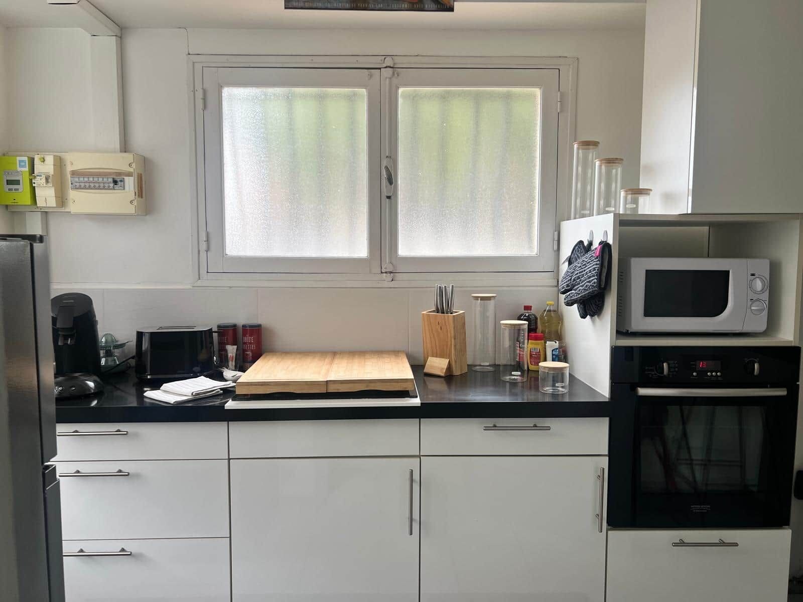 Een keuken met een raam, een magnetron, een koffiezetapparaat en kastjes.