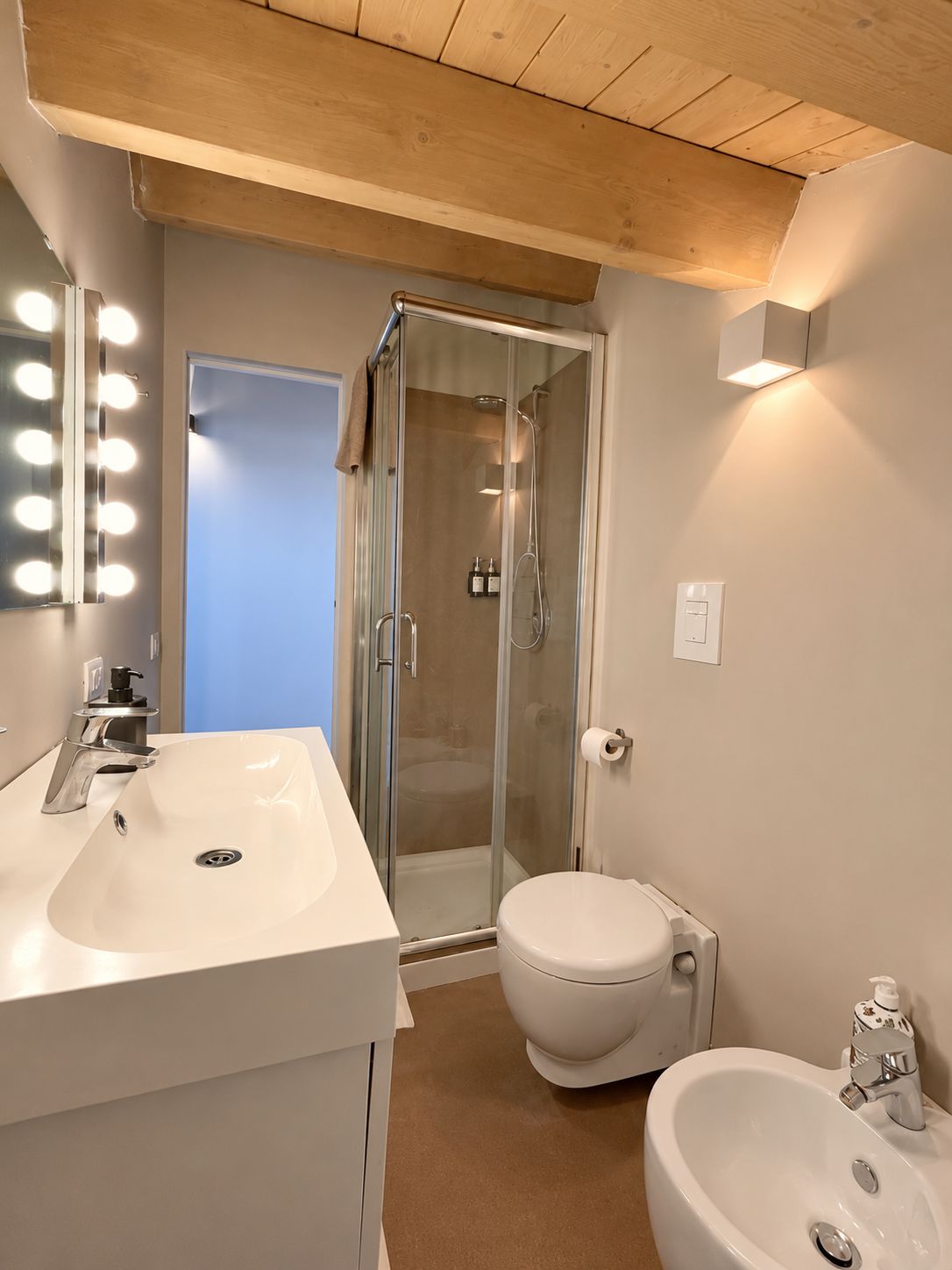 Ein Badezimmer mit Dusche, Toilette, Bidet und einem Waschtisch mit Spiegel und Beleuchtung.