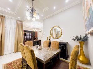 A dining area with a marble table, patterned chairs, a chandelier, a wall-mounted mirror, and a decorative vase. - AfriBella Executive Suite (Kumasi)