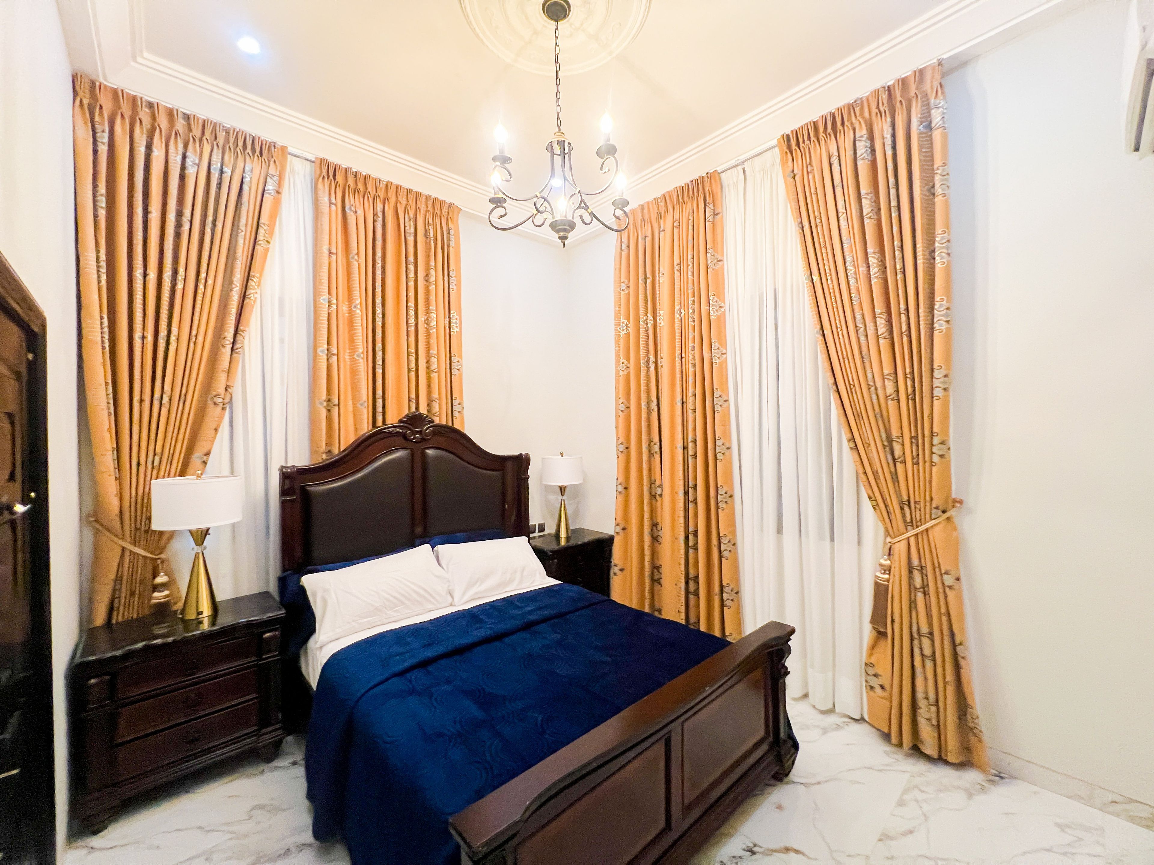 A bedroom with a bed, nightstands, a chandelier, and curtains.