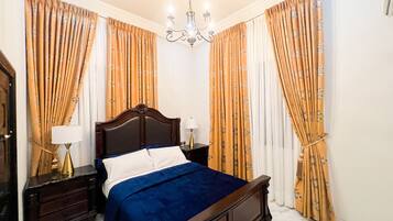 A bedroom with a bed, nightstands, a chandelier, and curtains.