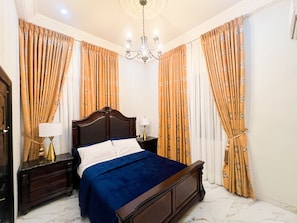 A bedroom with a bed, nightstands, a chandelier, and curtains. - AfriBella Executive Suite (Kumasi)