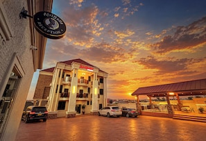 A hotel with a reception sign, multiple floors, and a parking area with cars. - AfriBella Executive Suite (Kumasi)