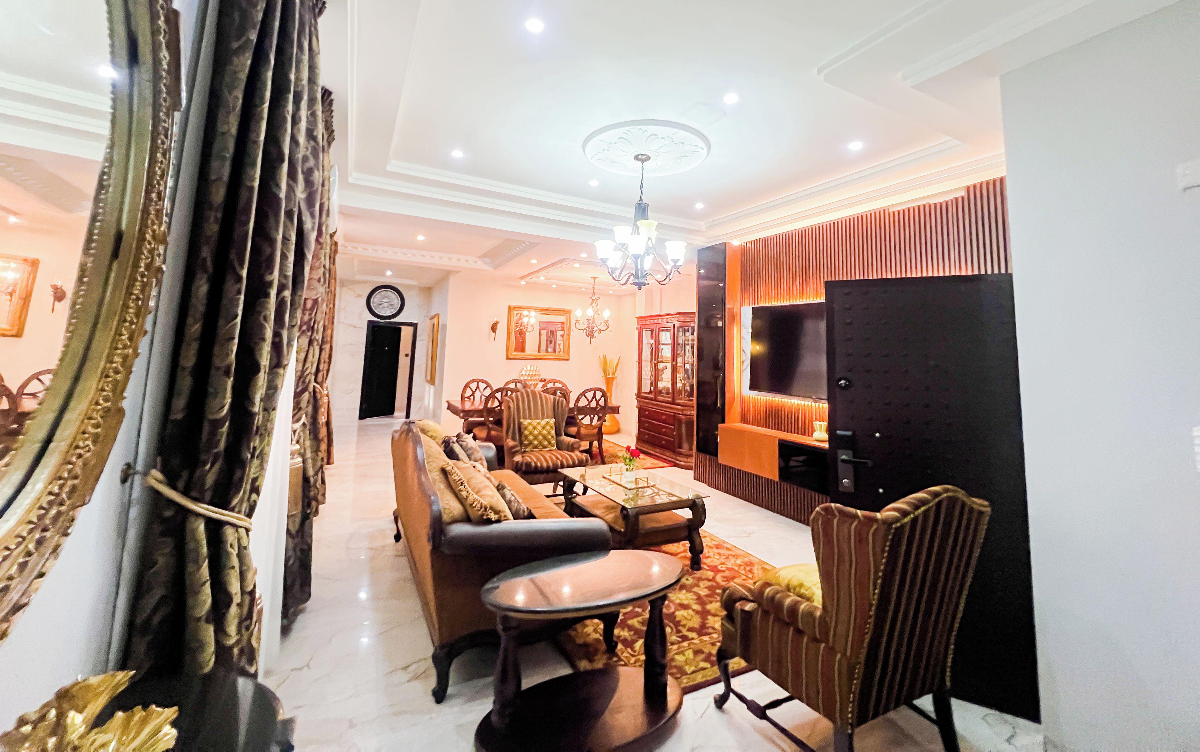 A well-lit living room with a sofa set, a dining table, and a TV.