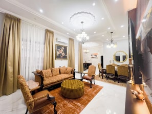 A spacious living room with a sofa set, ottoman, and dining area with chairs and a table. - AfriBella Executive Suite (Kumasi)