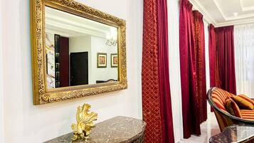 A room with a large ornate mirror, a marble console table with a golden lion sculpture, and red curtains.