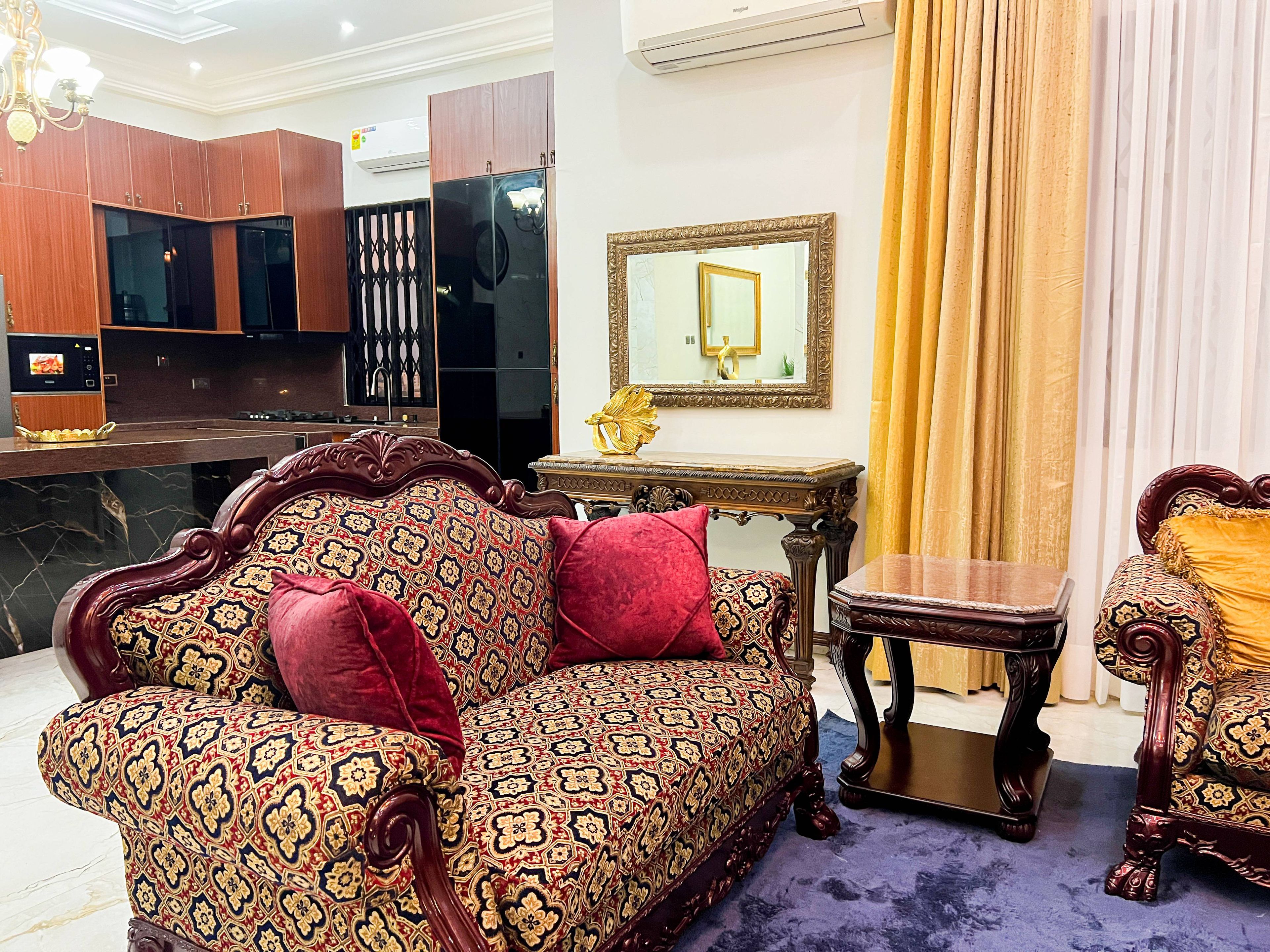 A room with a patterned sofa, a small table, a mirror, and a cabinet.