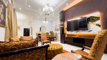 A well-lit living room with a chandelier, patterned sofas, a television, and a dining area with chairs and a table.