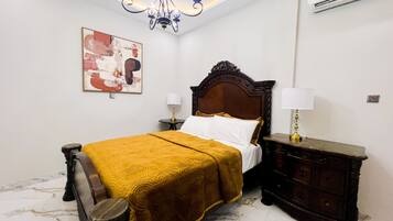 A hotel room with a bed, bedside tables, a chandelier, an air conditioner, and a painting on the wall.