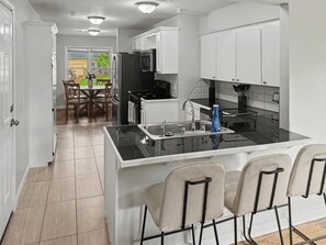 A modern kitchen with a central island, white cabinetry, and a dining area with a table and chairs. - Peaceful 3-bedroom house with AC in charming Broken Arrow (Broken Arrow)