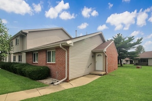 A two-story residential house with a brick facade, a front porch, and a well-maintained lawn. - Spacious 2BR Condo - UIUC, Carle + Free Parking (Champaign)
