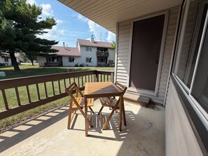 A wooden deck with a table and chairs, a covered area with a door, and a view of neighboring houses. - Spacious 2BR Condo - UIUC, Carle + Free Parking (Champaign)