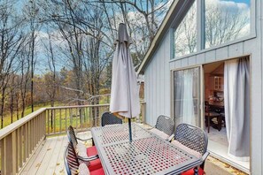 A deck with a table and chairs, an umbrella, and a view of trees and a building. - Vermont Chalet 10 Min to Mount Snow - Fireplace, Game Room & Fire Pit, Sleeps 10 (Wilmington)