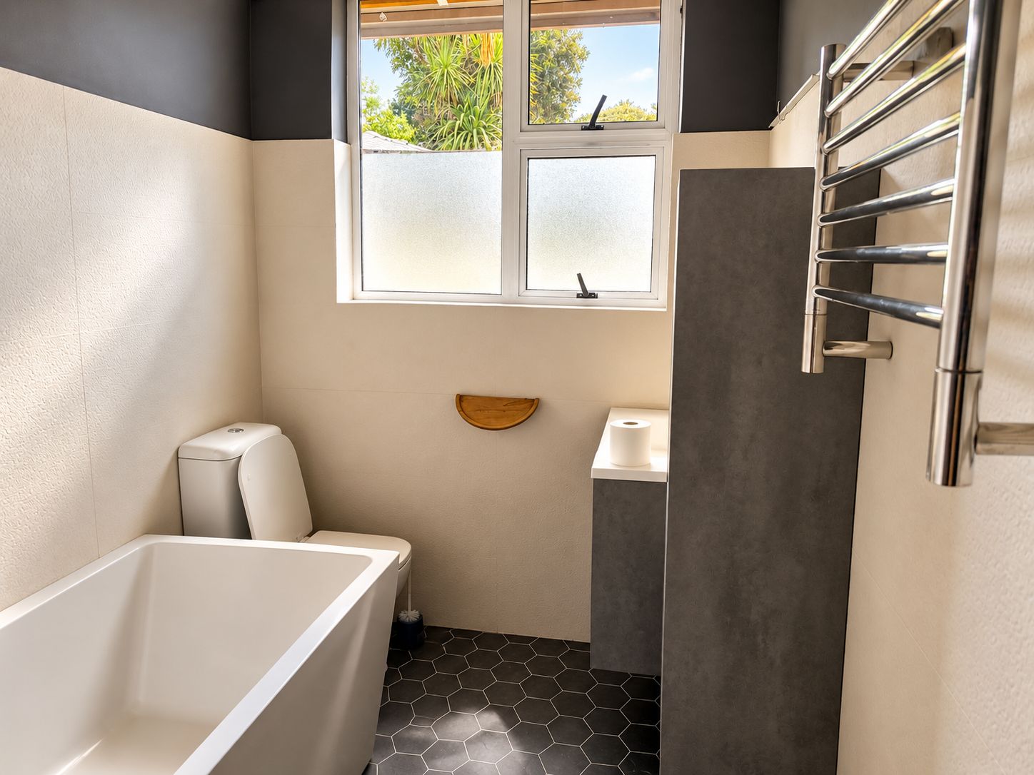 A bathroom with a bathtub, toilet, and a window with frosted glass.