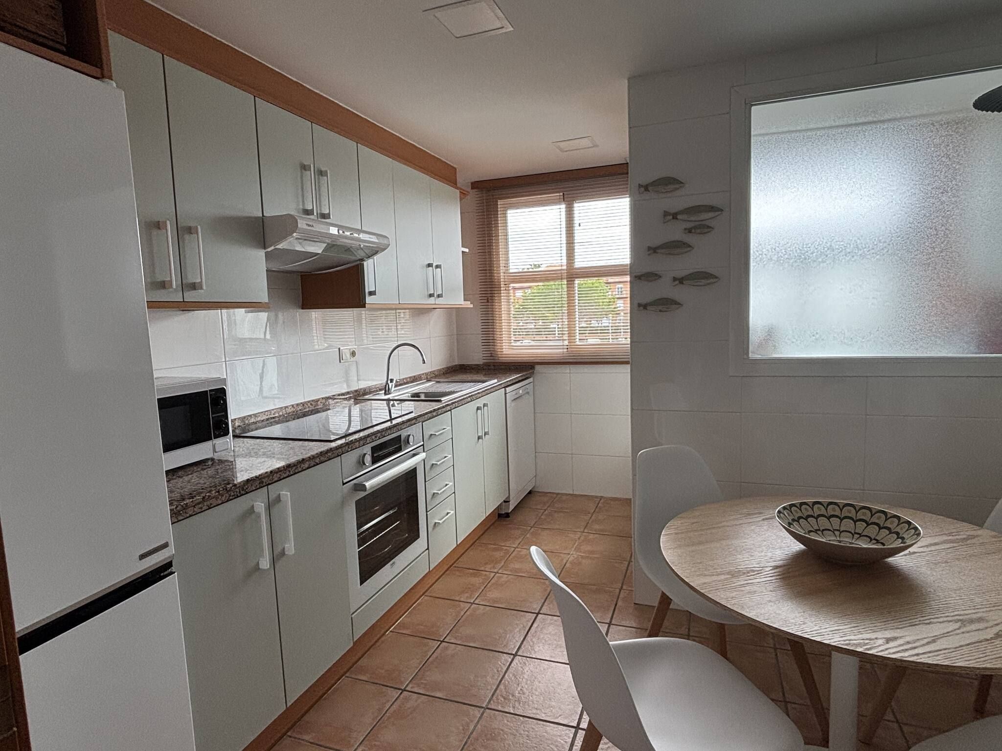 Una cocina con armarios blancos, estufa, lavabo y ventana con persianas.