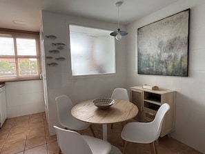 A dining area with a round table, four chairs, a bowl, a fish decoration, a painting, and a window with blinds. - L'oneta Mediterranean Charm by the sea (Javea)