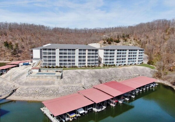 A large hotel with multiple floors, a dock with boats, and a hilly forested background. - Lakefront condo at lake of the ozarks (Lake Ozark)