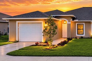 A residential house with a garage, a small tree, and a well-maintained lawn. - 2025 Waterfront 3/2 Canal Views, Garage, Laundry (Cape Coral)