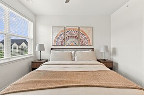 Ein Schlafzimmer mit einem Bett, zwei Nachttischen, einem Fenster mit Jalousien und drei an der Wand befestigten Kunstwerken.