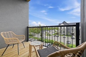 Ein Balkon mit Korbmöbeln, einem Glastisch und Blick auf einen Parkplatz sowie Gebäude.